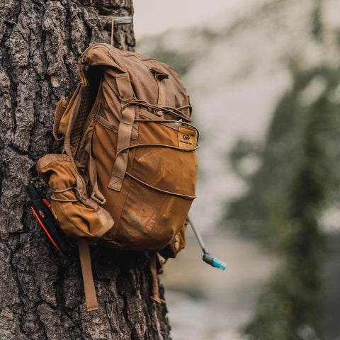 Brown Adventure Pack 12L hanging on a tree with the bladder hose out