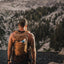 Back view of the brown Adventure Pack 12L on a hiker with a bottle in the side pocket