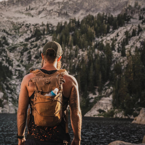 Back view of the brown Adventure Pack 12L on a hiker with a bottle in the side pocket