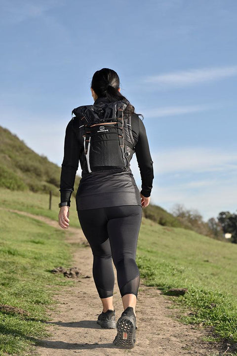 Woman hiking a trail wearing the black Adventure Pack 12L, back view