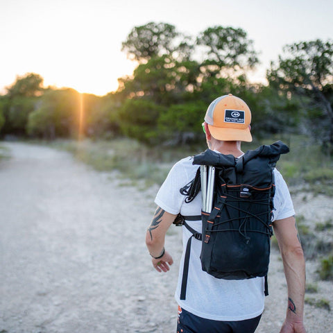 Man walking a trail at sunset wearing the black Adventure Pack 20L